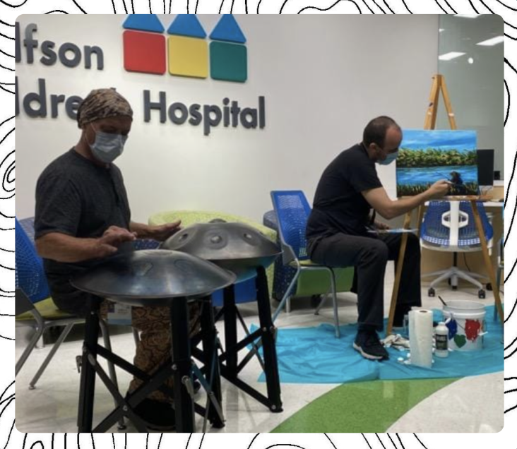 Two artists, one playing handpans, the other painting a picture
